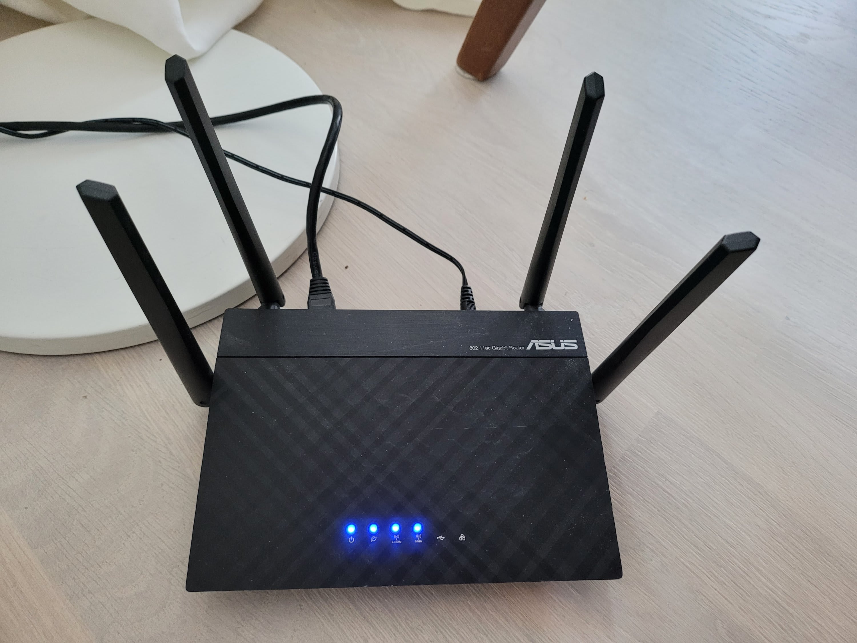 En svart Asus-router med fyra antenner och blå indikatorlampor står på ett ljust golv.