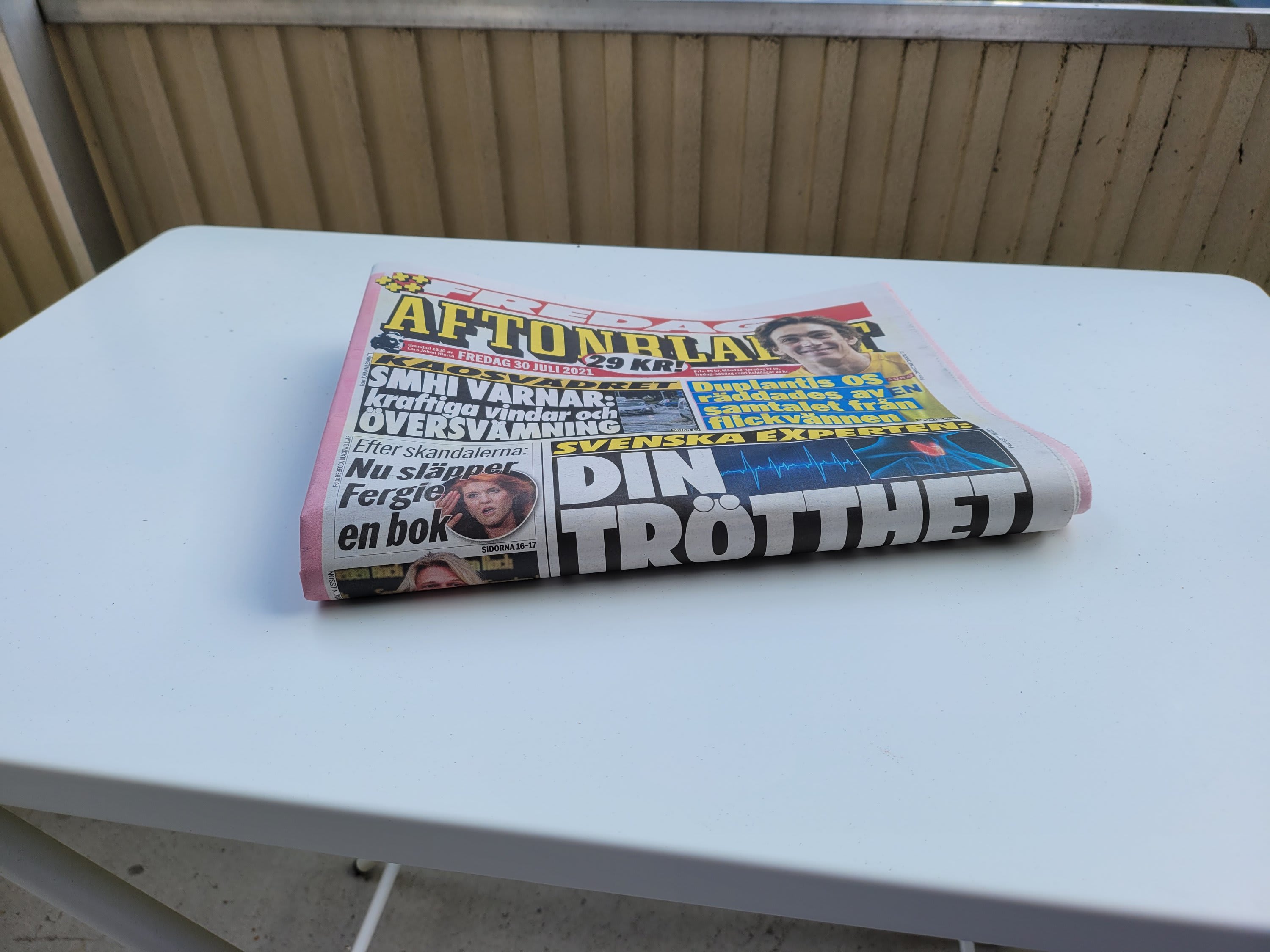 En vikt papperstidning från Aftonbladet ligger på ett vitt bord framför ett räcke.