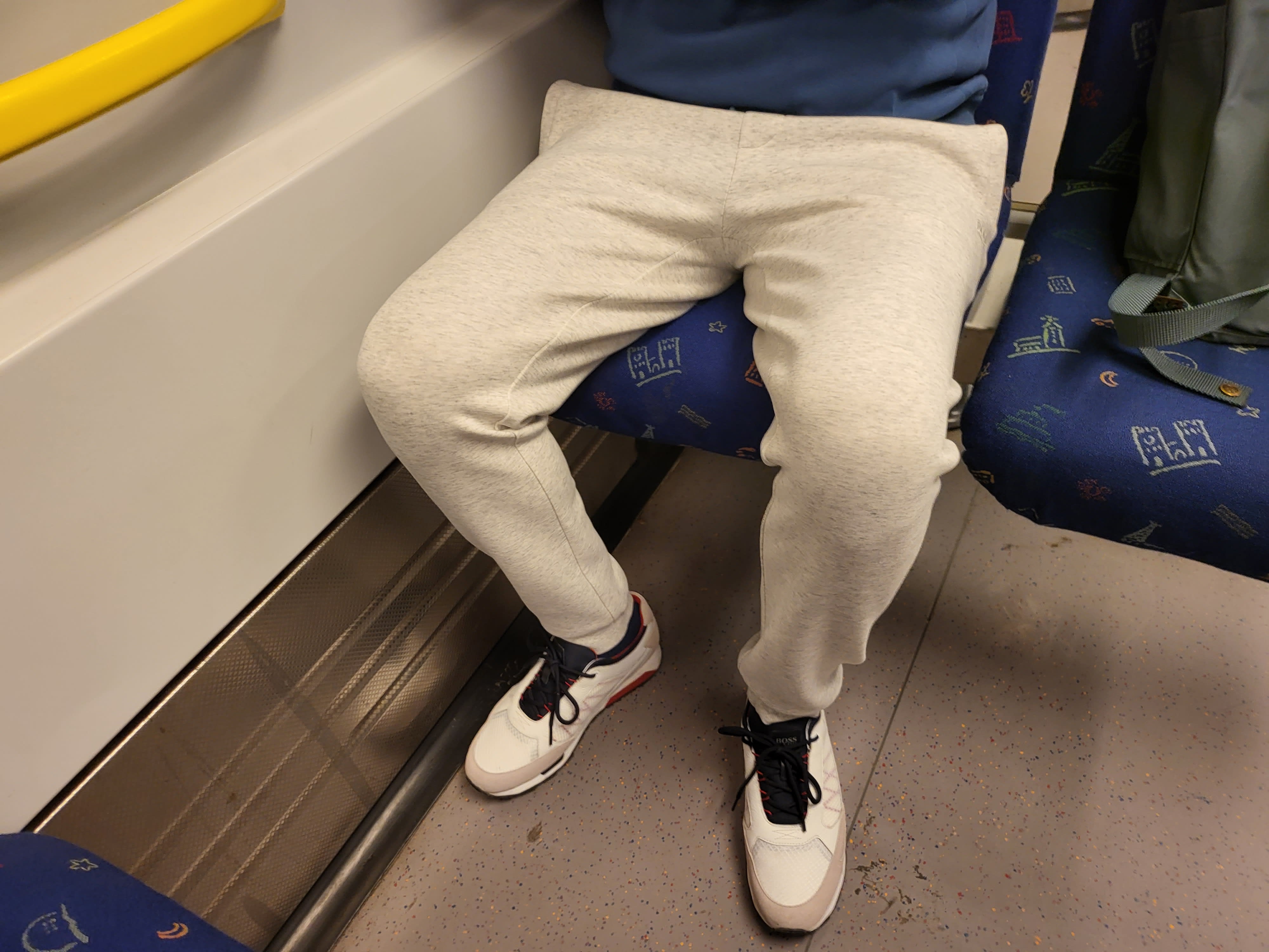En person i ljusgrå mjukisbyxor och vita sneakers sitter på ett blåmönstrat säte.